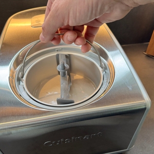 Eine Hand hält den Griff des Behälters der Cuisinart ICE100E fest.