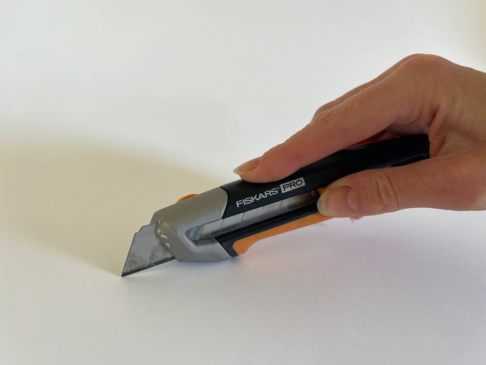 Eine Hand hält ein getestetes Cuttermesser mit ausgefahrener Klinge.