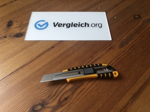 Cuttermesser liegt auf einem Holztisch mit einem Vergleich.org-Schild daneben
