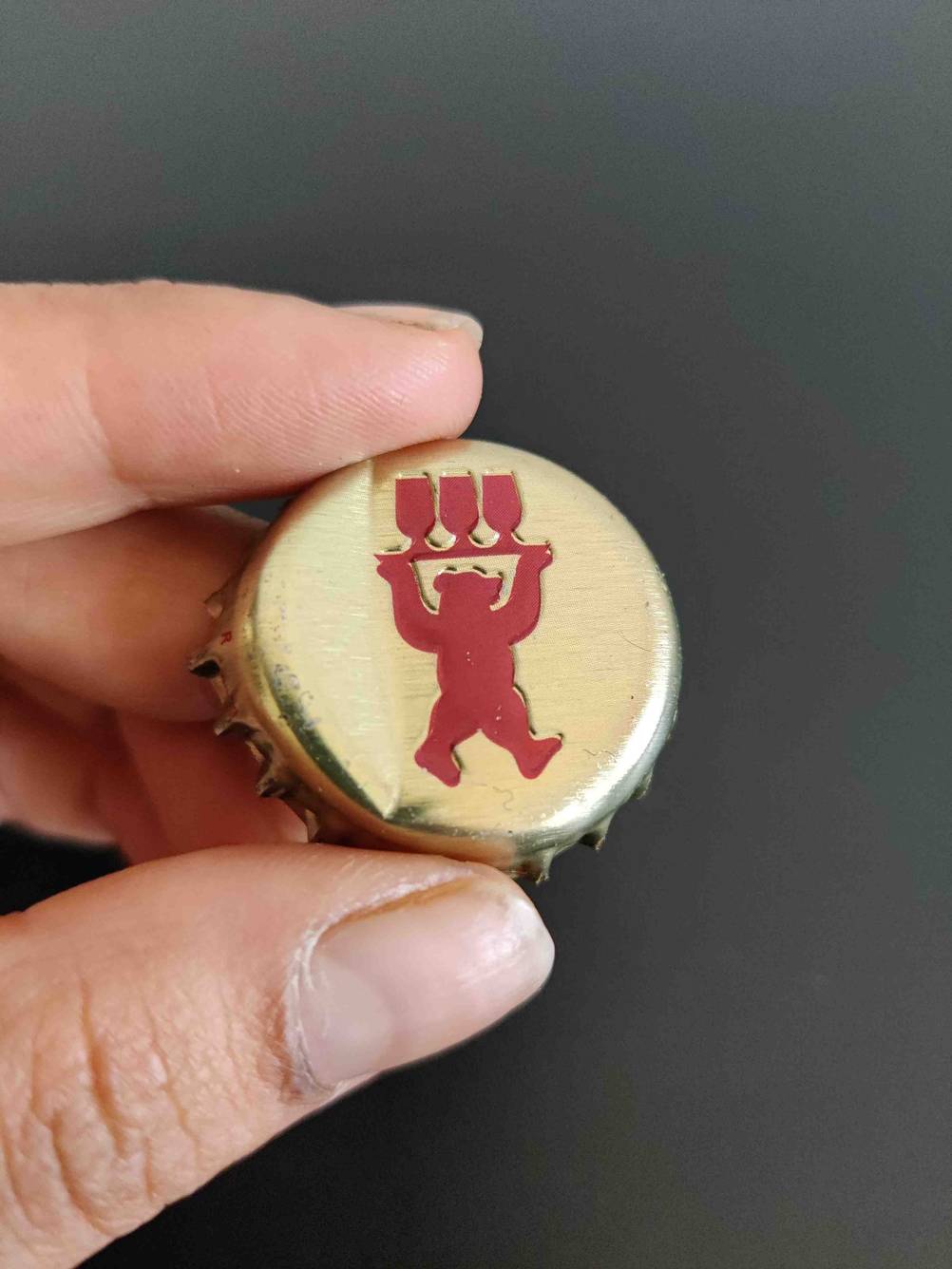 Eine Hand hält den Kronkorken einer Flasche des getesteten Biers vor eine dunkle Fläche.