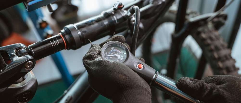 Nahaufnahme eines Mechanikers, der den Druck eines Fahrraddämpfers mit einer Dämpferpumpe einstellt.
