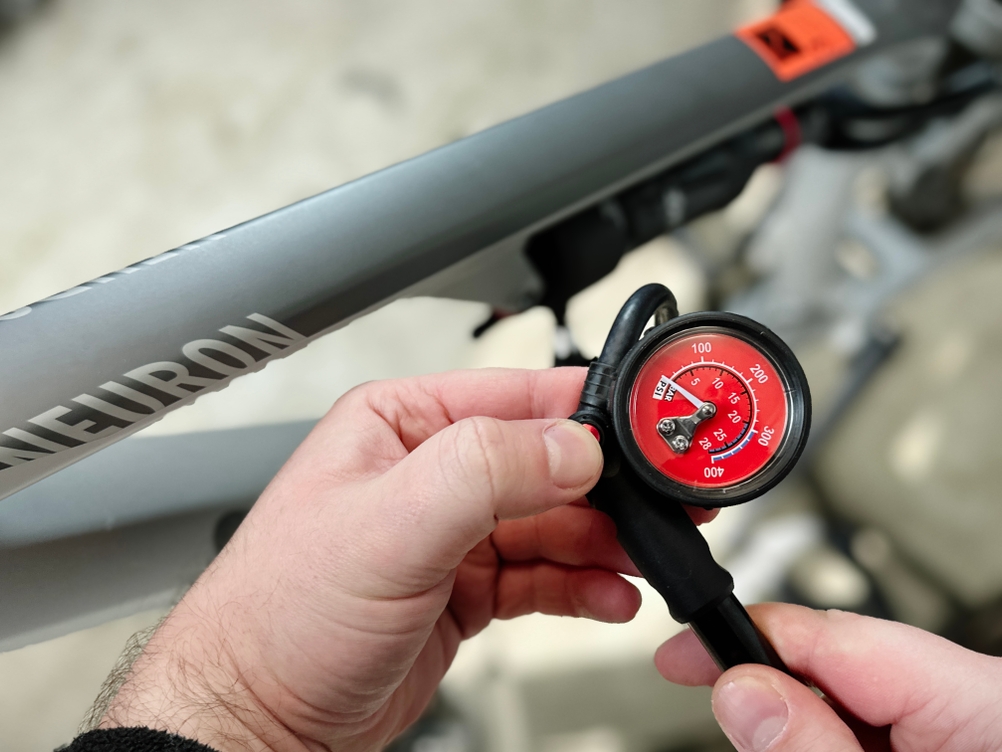 Die Hand hält die rote Druckanzeige der Pro Bike Tool BSP-01 direkt am Fahrradrahmen. Der Schlauch führt zum Hinterbaudämpfer.