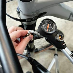Die SKS-SAM-Dämpferpumpe wird an ein Mountainbike angeschlossen. Die Hand hält den flexiblen Schlauch beim Aufsetzen auf das Ventil.