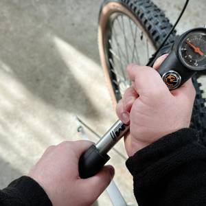 Zwei Hände bedienen die SKS-SAM-Dämpferpumpe am Fahrrad. Die Anzeige zeigt den aktuellen Druck.