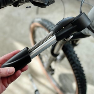 Die SKS-SAM-Dämpferpumpe liegt zusammengeklappt auf einer Werkbank. Der Schlauch ist vollständig verstaut.