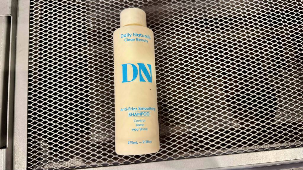Im Test: Ein Anti-Frizz-Produkt in der Kunststoffflasche liegt auf einem Regalgitter.