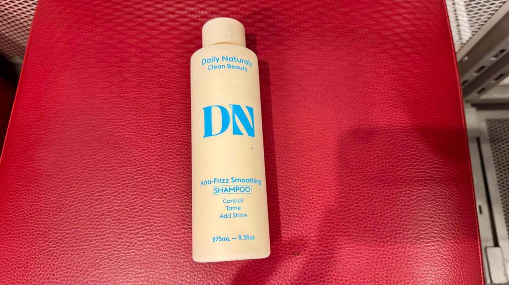 Ein getestetes Anti-Frizz-Produkt in der Kunststoffflasche liegt auf einem roten Hocker.