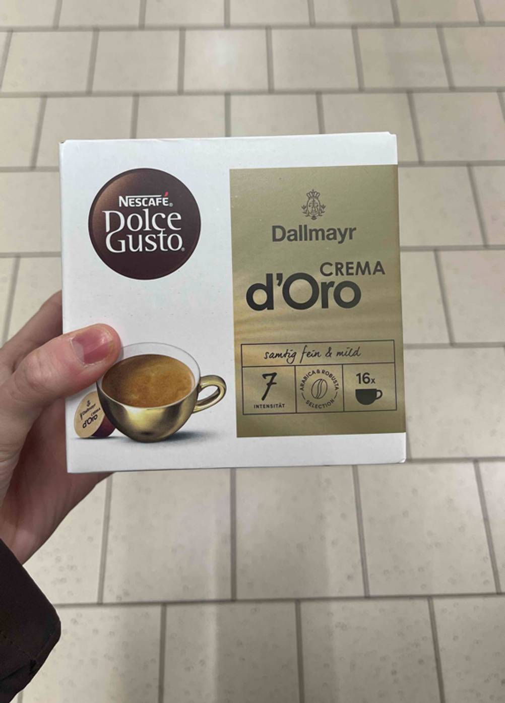 Im Test: Die Dallmayr-Kapseln der Geschmacksrichtung Crema d’Oro befinden sich in einem weiß-goldenen Karton, der in einer Hand gehalten wird.