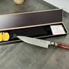 Das Fanteck Gyuto liegt ausgepackt in einer offenen Box. Die Verpackung enthält Zubehör wie einen Klingenschutz, ein Reinigungstuch und einen kleinen Messerschärfer.