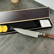 Das Fanteck Gyuto liegt ausgepackt in einer offenen Box. Die Verpackung enthält Zubehör wie einen Klingenschutz, ein Reinigungstuch und einen kleinen Messerschärfer.