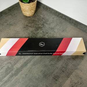 Die geschlossene Produktverpackung des Fanteck 8'' Executive Chef Knife liegt auf einer Küchenarbeitsplatte. Das Design ist in Schwarz, Weiß, Rot und Gold gehalten.