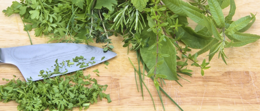 Ein Damastmesser liegt neben Kräutern auf einem Schneidebrett.
