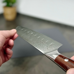 Das Schneidwerk-Santoku-Messer wird aus seitlicher Perspektive gehalten. Klingenmuster, Schliff und Griff sind klar zu erkennen.