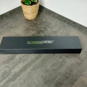 Die geschlossene Verpackung des Schneidwerk-Santoku-Messers liegt auf der Küchenarbeitsfläche. Das Design ist schlicht in Schwarz gehalten.