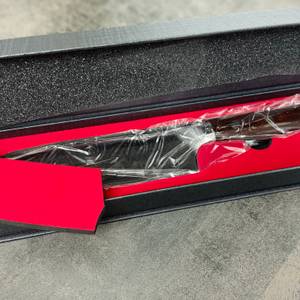Die Innenverpackung des Schneidwerk-Santoku-Messers zeigt das Messer in einer roten Schaumstoffeinlage. Es ist noch in Schutzfolie eingewickelt.