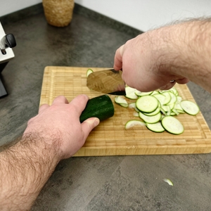 Das Schneidwerk-Santoku-Messer liegt auf einem Schneidbrett neben geschnittener Zucchini. Die Spitze zeigt Richtung Kamera.