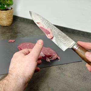 Ein Stück Fleisch mit Fettrand wird mit dem Schwartzhirsch Caliburn geschnitten. Der Schnitt verläuft entlang des Fettgewebes.