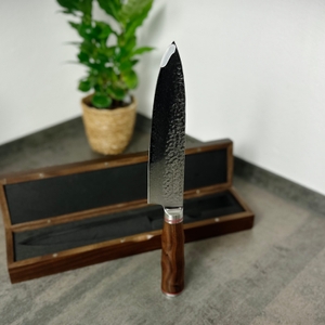 Das Schwartzhirsch Caliburn steht senkrecht auf dem Griff, die Klinge zeigt nach oben. Im Hintergrund ist die Holzbox leicht geöffnet.