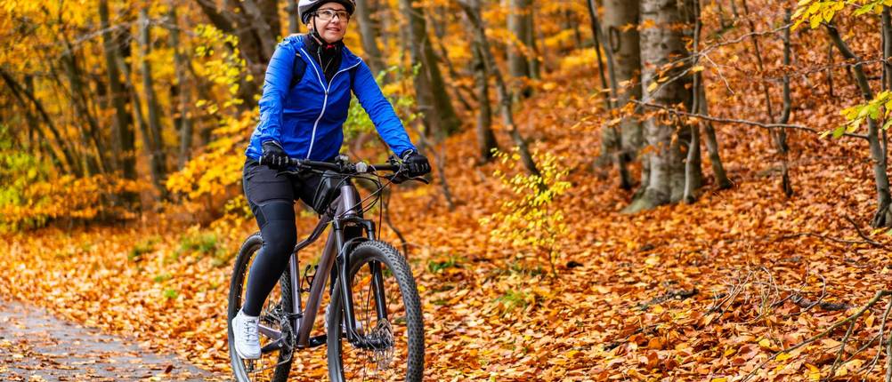 3/4-Radhosen-Damen-Test: Eine Frau in langer Radlerhose fährt durch den herbstlichen Wald. Orange Blätter liegen am Boden.