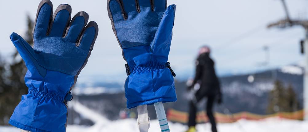 Damen-Skihandschuhe-Test: Blaue Skihandschuhe stecken auf Skistöcken im schneebedeckten Skigebiet. 