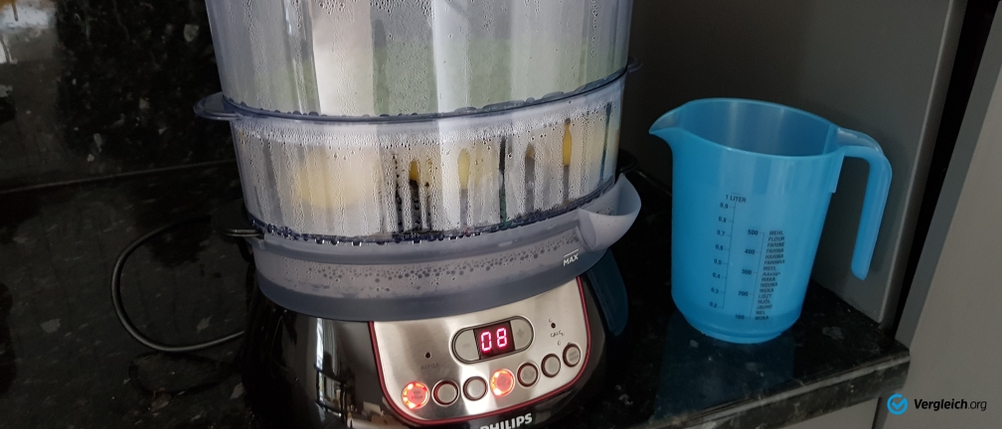 Dampfgarer von Philips steht auf einer dunklen Arbeitsfläche, daneben ein Messbecher mit Wasser