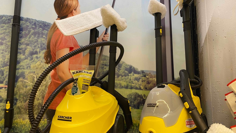 Zwei getestete Dampfreiniger vor einem Plakat in einer Verkaufsfläche.