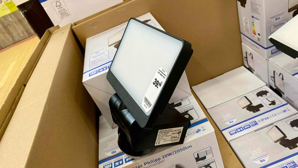 Seitenansicht auf einen rechteckigen Darius LED-Strahler im Test, der über IP-Schutz 44 und einen Bewegungsmelder verfügt und inklusive Preisetikett auf Verpackungen des gleichen Modells lehnt.