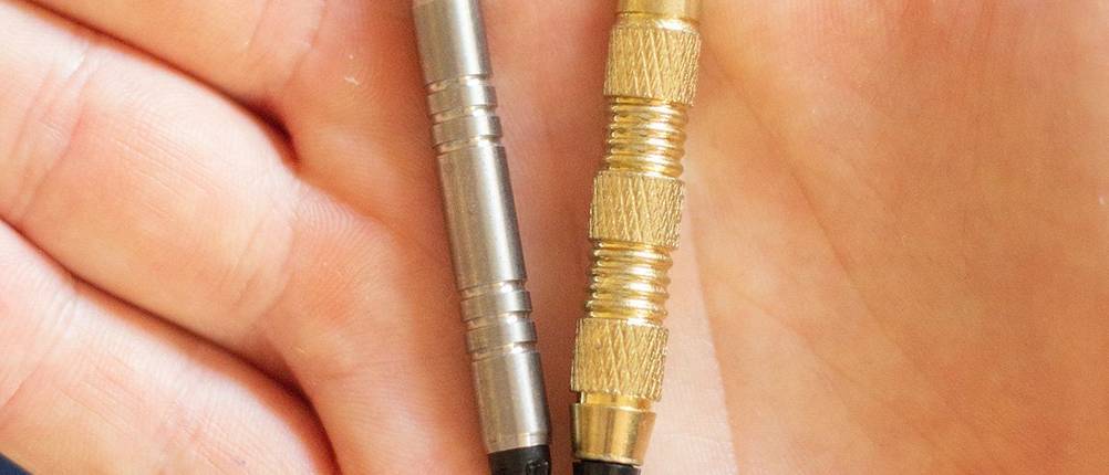 Dartpfeile im Test: ein Dartpfeil mit Griffstück aus Wolfram (links) und einer mit Griffstück aus Messing (rechts) auf der Handfläche präsentiert