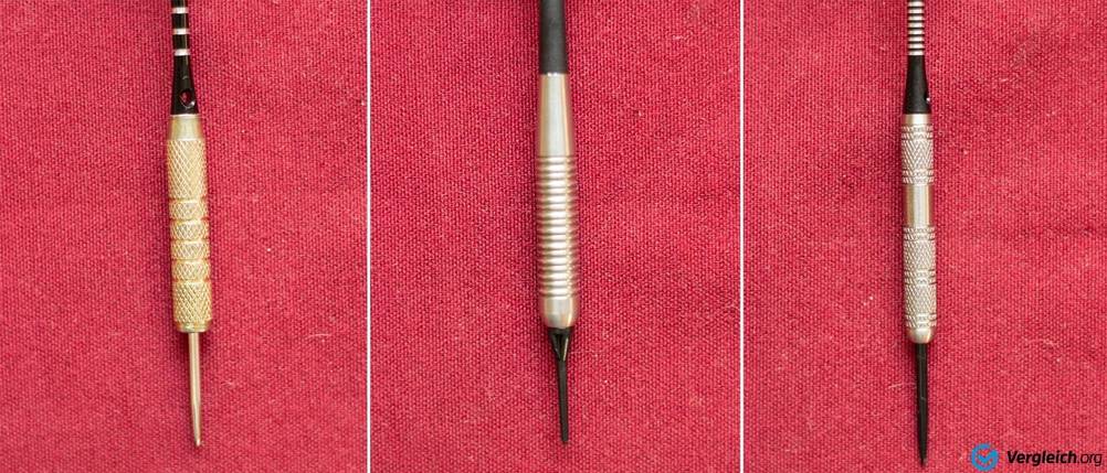 Dartpfeile im Test: Nahaufnahme von drei verschiedenen Griffstücken von Dartpfeilen auf rotem Untergrund (links: Messing, mittig: Stahl, rechts: Wolfram)