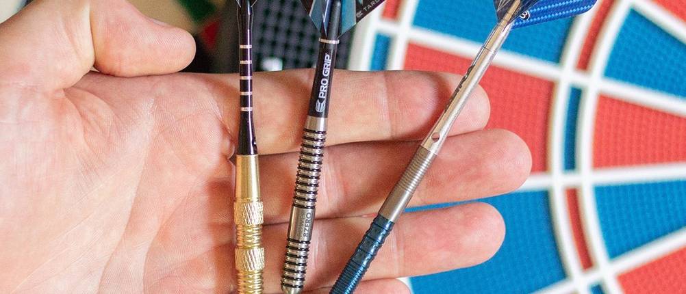 Dartpfeile im Test: drei verschiedene Dartpfeile auf der Handfläche präsentiert, im Hintergrund eine Dartscheibe