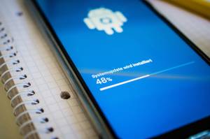 Datenrettungsprogramme im Test: Ein Smartphone liegt auf einem Collegeblock, auf dem Display wird der Fortschritt eines Systemupdates angezeigt.