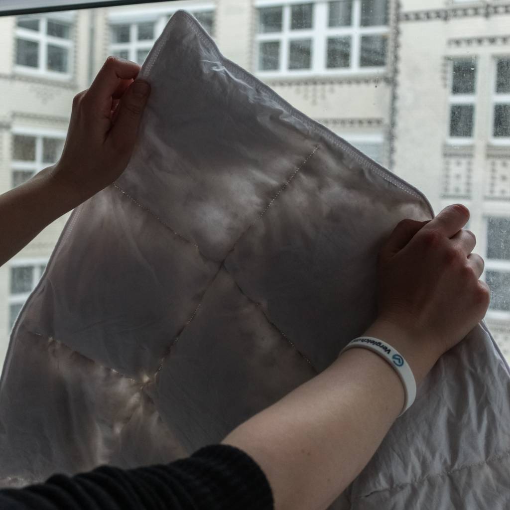 Eine Daunendecke wird vor ein Fenster gehalten.