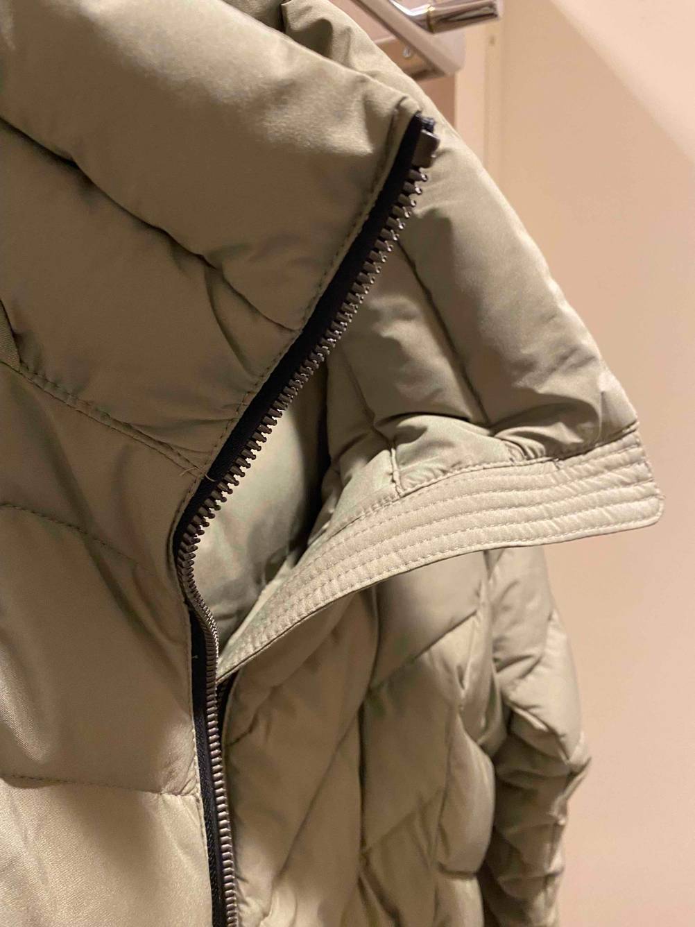 Damen-Daunenjacke im Test. Nahaufnahme eines Reißverschlusses einer beigefarbenen Daunenjacke.