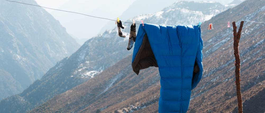 Daunenschlafsack-Test: blauer Schlafsack und Socken hängen auf einer Wäscheleine in den Bergen.