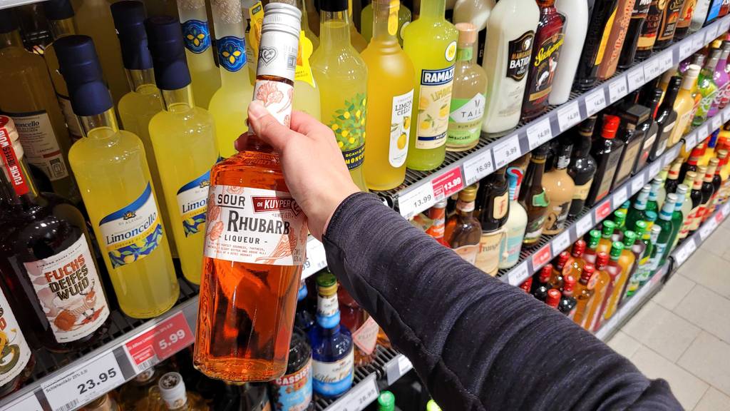 Rhabarberlikör-Test: Eine Hand hält eine Flasche vor einem Verkaufsregal.