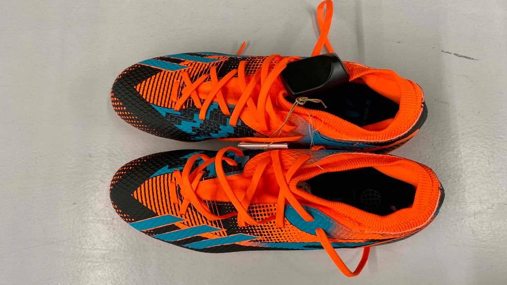Im Test: Ein Paar Fußballschuhe für Herren in orange-schwarz-blauem Design steht auf hellem Untergrund.