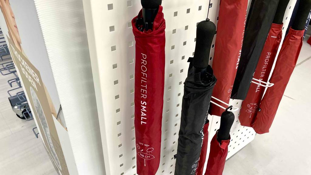 Golfschirme im Test: Mehrere rote und schwarze Golfschirme mit Lichtschutzfaktor 50+ hängen an einem Verkaufsstand.