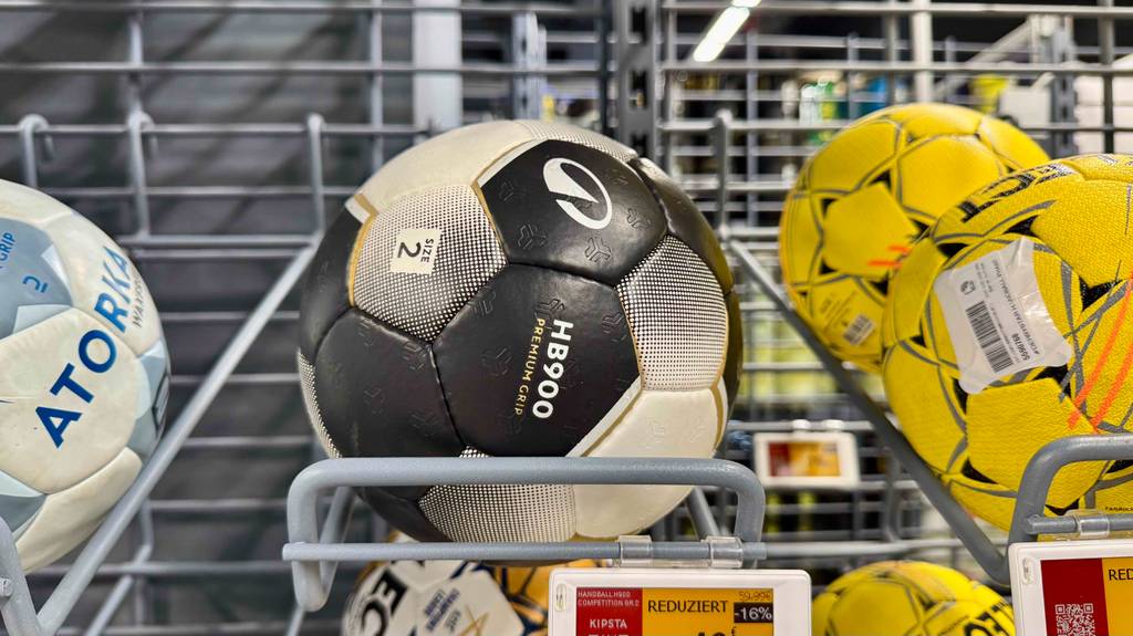 Ein Handball in Größe 2 liegt zum testen in einem Ballregal zwischen anderen Bällen.