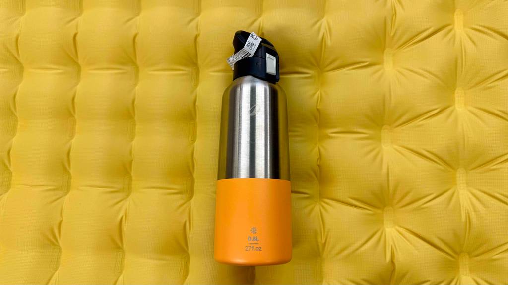 Eine Isolierflasche aus Edelstahl liegt zum testen auf einer gelben Luftmatratze.