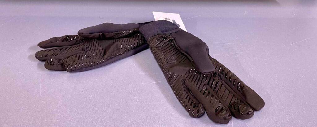 Getestete Touchscreen-Handschuhe mit grifffesten Gummi-Applikationen auf dem Handinneren liegen ausgebreitet auf einer lilafarbenen Oberfläche.