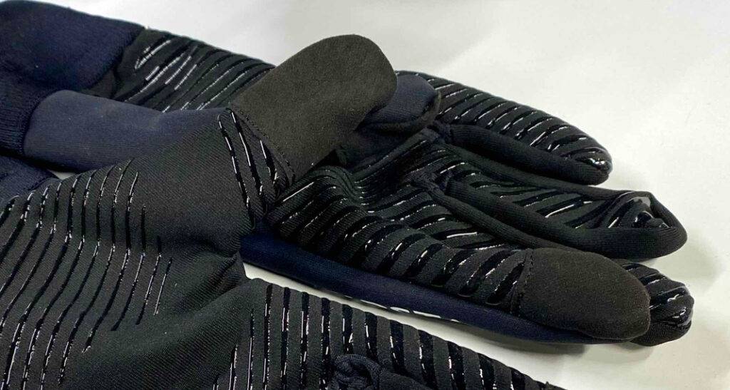 Im Test: Touchscreen-Handschuhe in Blau-schwarz mit grifffesten Applikationen auf dem Handinneren liegen auf einer weißen Oberfläche.