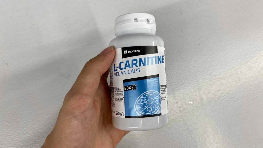 Im Test: Hand hält eine Dose Decathlon L-Carnitin vor weißer Wand.