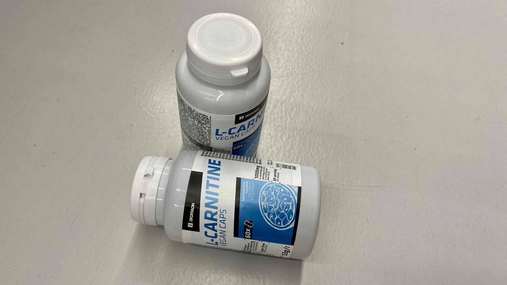 Im Test: eine Dose L-Carnitin von Decathlon liegt quer vor einer stehenden auf weißer Fläche.