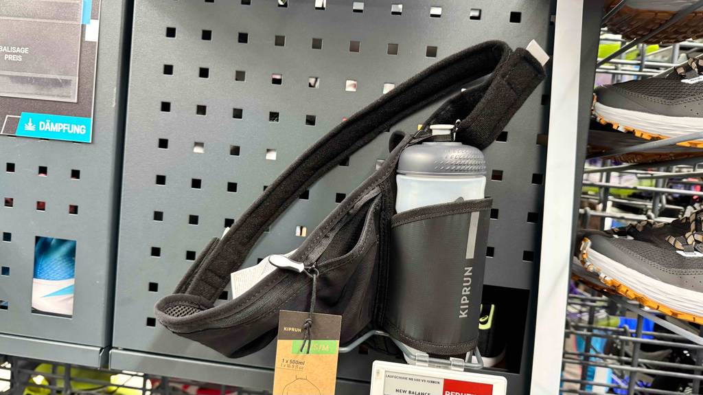 Ein getesteter Laufgürtel mit Trinkflasche steht in einem Gitterregal neben Schuhen.