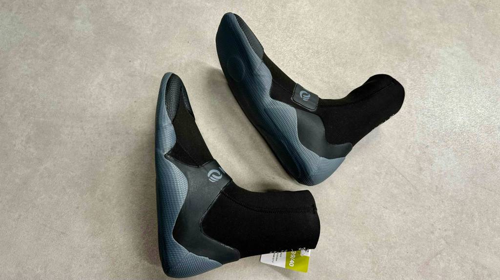 Zwei getestete Neoprenschuhe für Damen liegen seitlich übereinander auf einem hellen Boden.