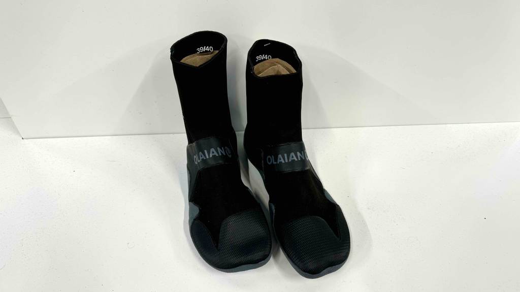 Ein Paar schwarze Neoprenschuhe für Damen steht zum Testen vor einer weißen Wand.
