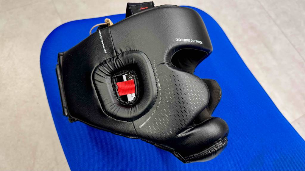 Auf einer blauen Matte liegt der getestete Kopfschutz für das Boxen aus schwarzem Kunstleder.