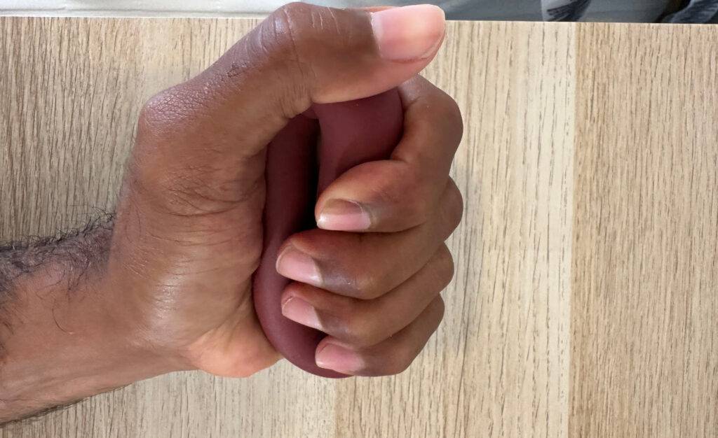 Handtrainer-Test: Hand quetscht einen dunkelroten Handtrainer über einer Holzfläche.