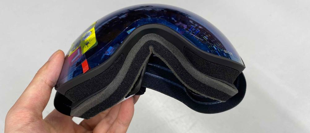 Skibrillen im Test: Hand hält eine Skibrille von unten vor weißer Wand.