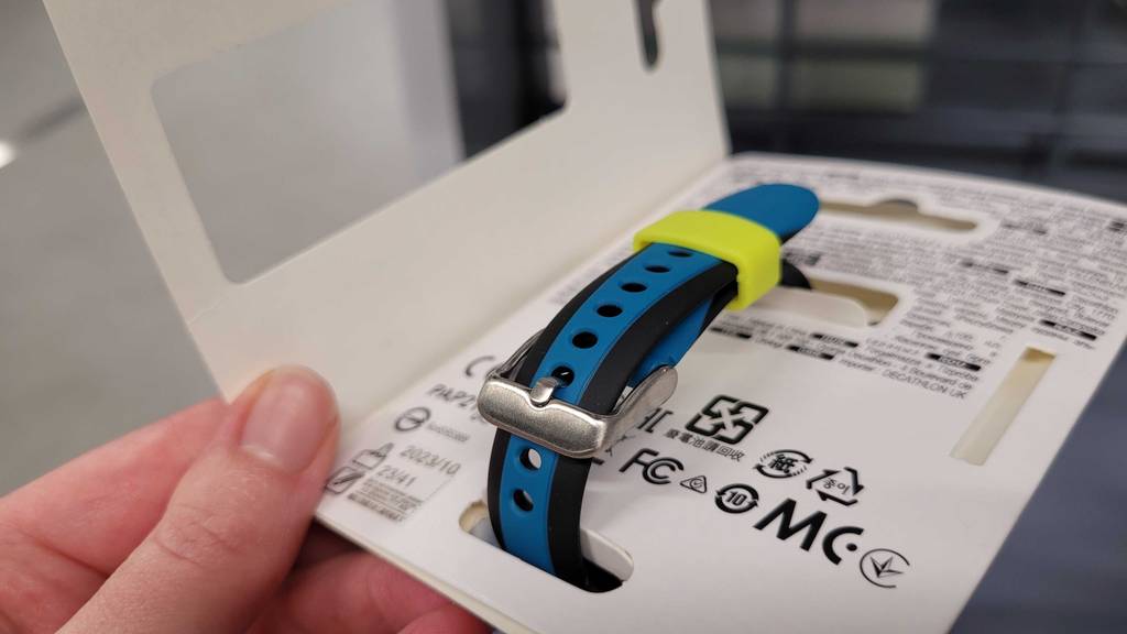 Hand zeigt die Innenseite eines weißen Verpackungskartons mit einem blau-schwarzen Armband inklusive giftgrüner Lasche sowie einer Metall-Schnalle.